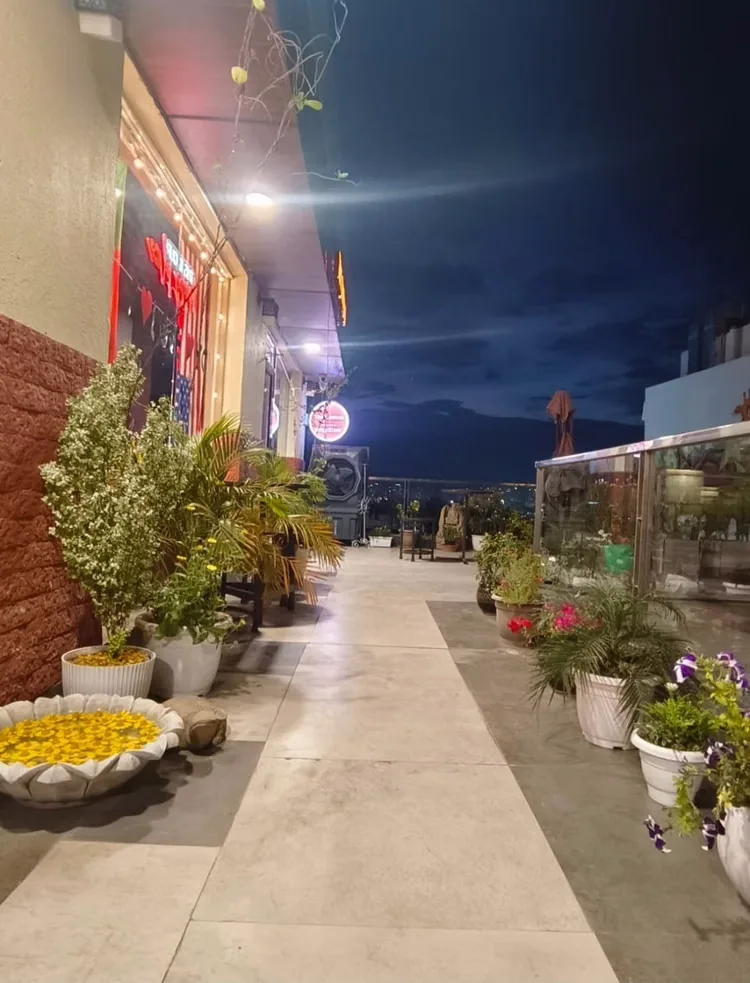 Open-air terrace corridor at night with planters and city lights beyond the glass railing
