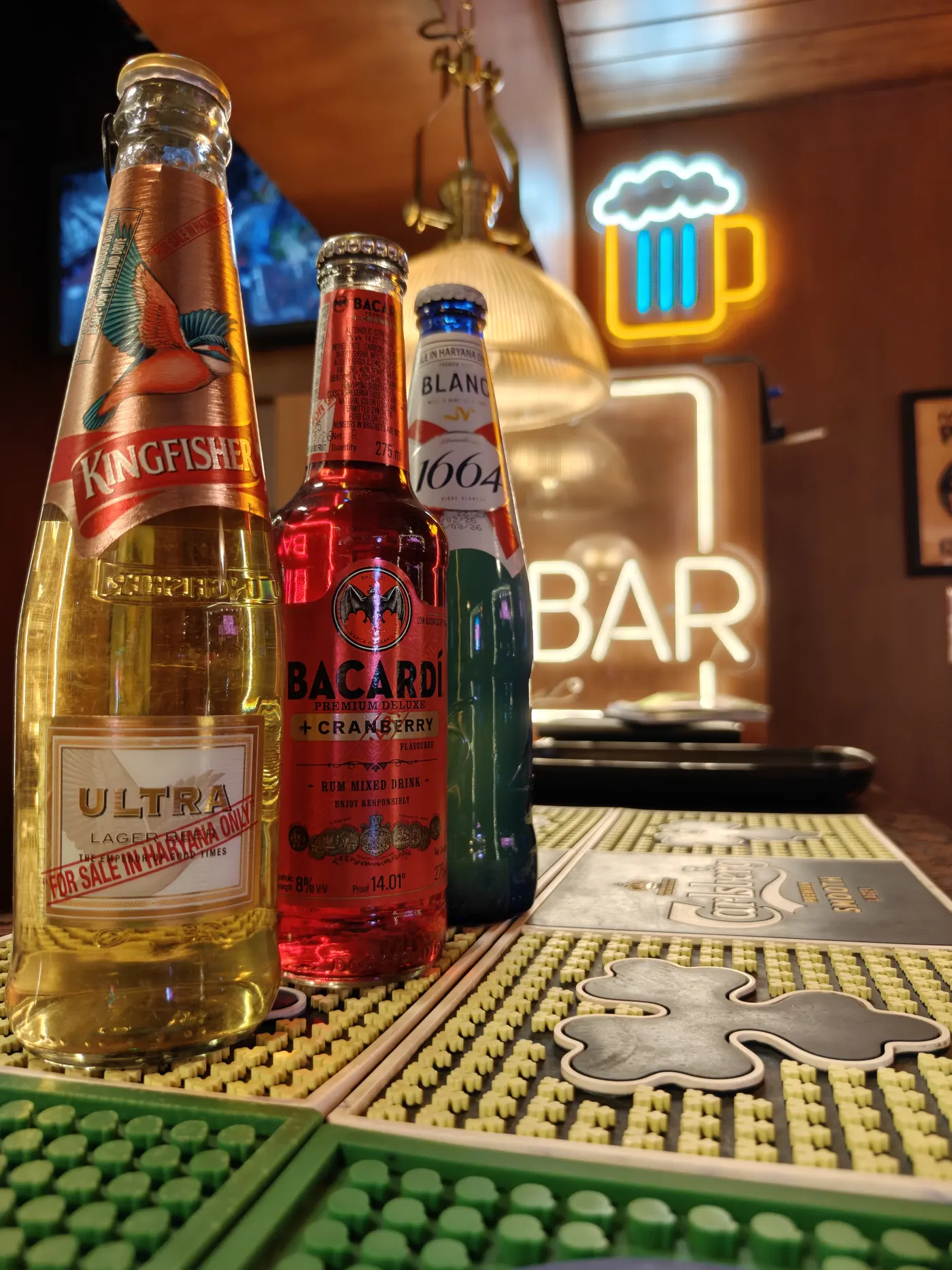 Chilled beer bottles lined up under the BAR neon